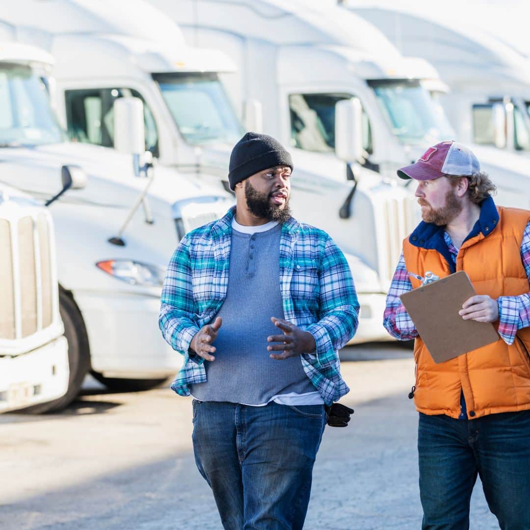Picture of 2 drivers talking with a fleet of trucks in the background. Freight consolidation.