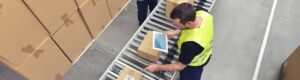A man with an iPad on a production line taking inventory of boxes on roller trays.