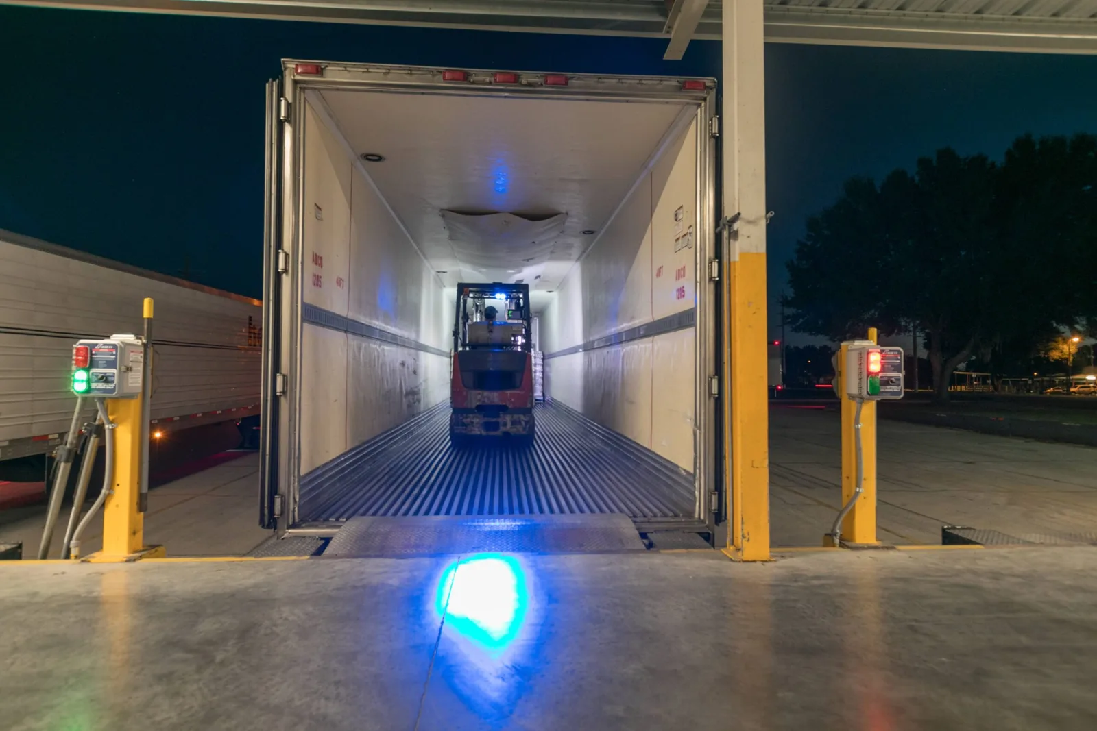 Forklift driving into a trailer at a CWI warehouse loading dock at night to load pallets directly onto the truck