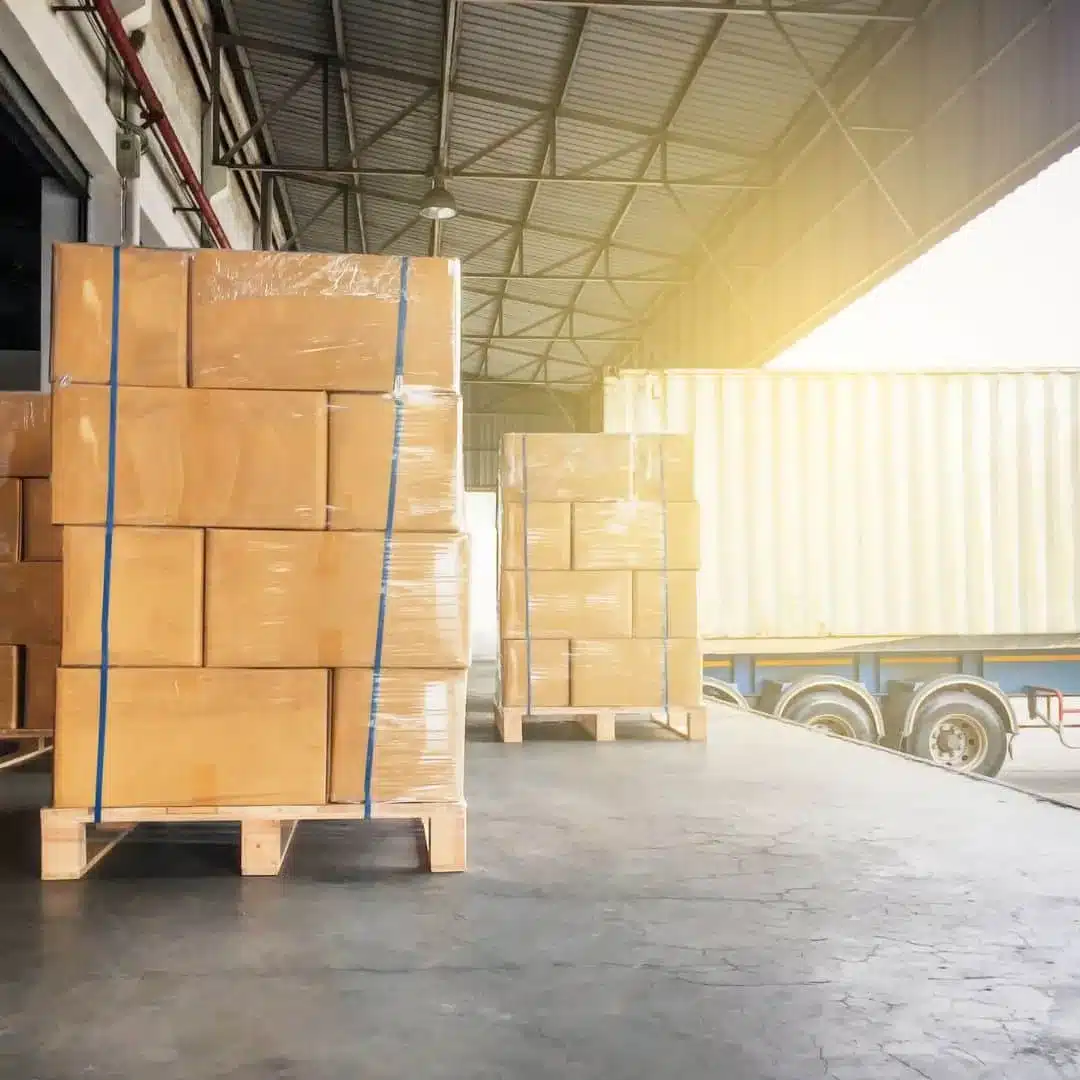 Wrapped pallets of boxed product staged at a warehouse loading dock next to a trailer, a sign of overflow storage